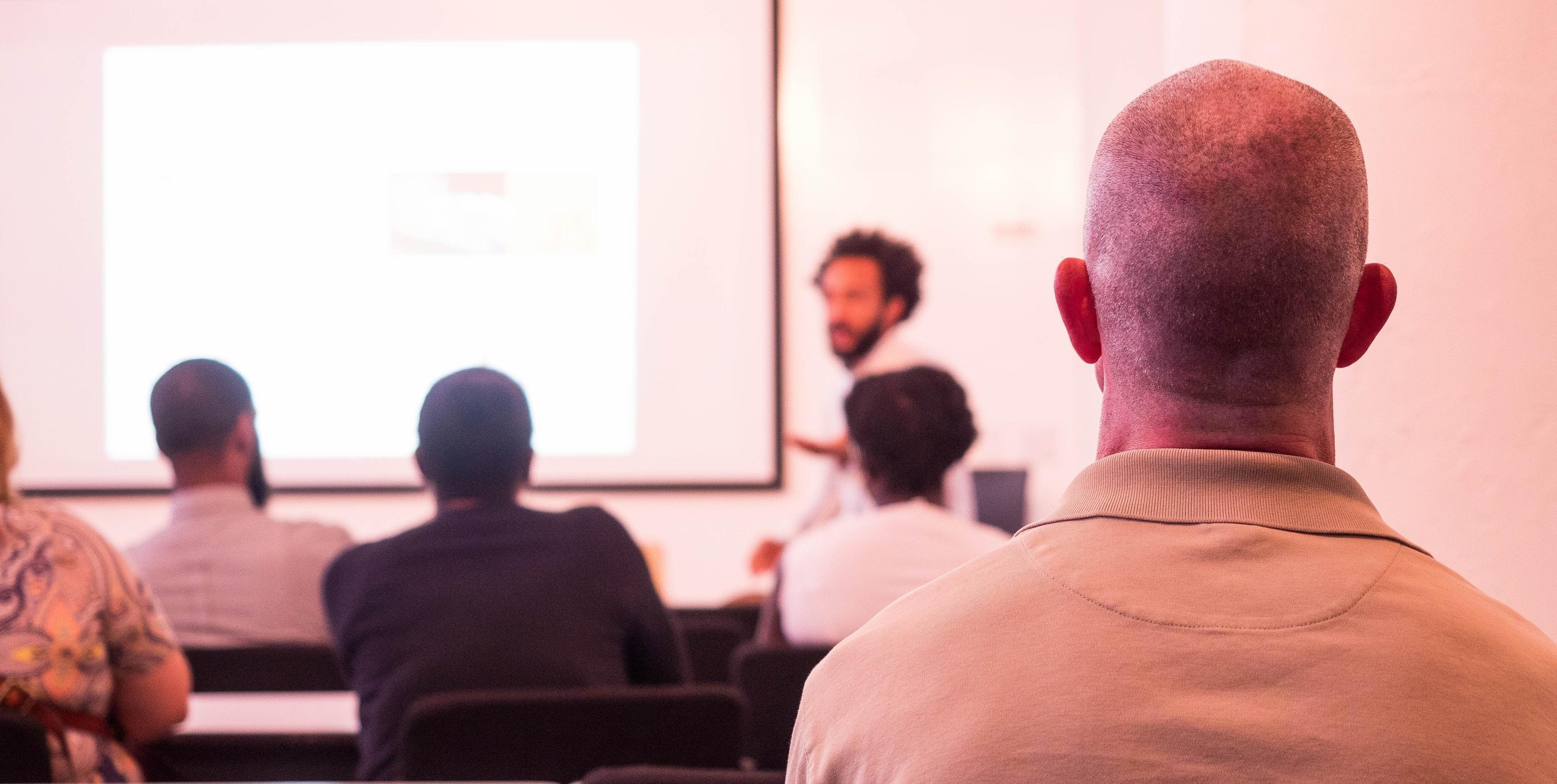 An instructor leading a technical workshop with students engaged in the foreground.